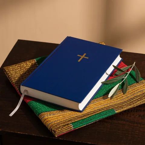 Bible à couverture bleue ornée d'une croix dorée, posée sur un tissu kente