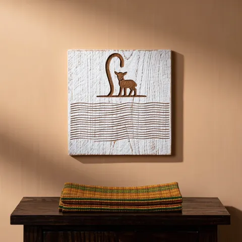 Plaque murale en bois blanchi gravée d'un bâton de berger et d'un agneau, accrochée au-dessus d'un tissu kente